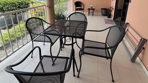 Un balcon avec une table et des chaises, un ventilateur de plafond et une vue sur la verdure et les bâtiments.