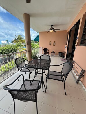 A balcony with a table and chairs, a ceiling fan, and a view of greenery and buildings. - Apartment in Boqueron (Cabo Rojo)
