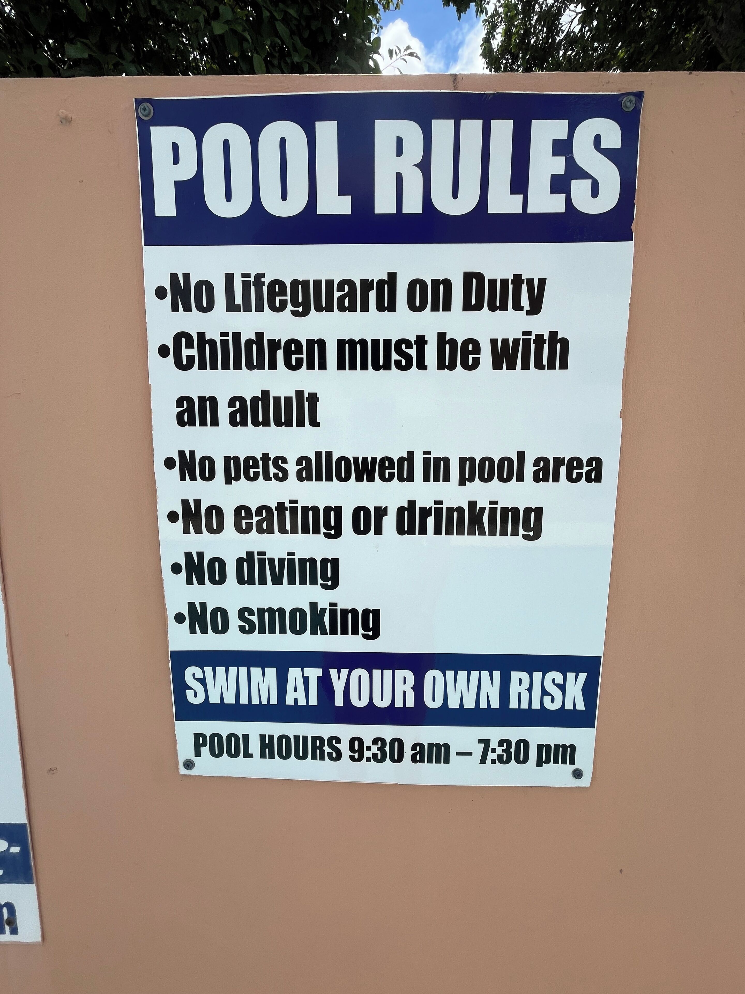A sign listing pool rules including no pets, no eating or drinking, and no diving.
