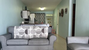Un salon avec un canapé gris, un tapis à motifs et une cuisine en arrière-plan.