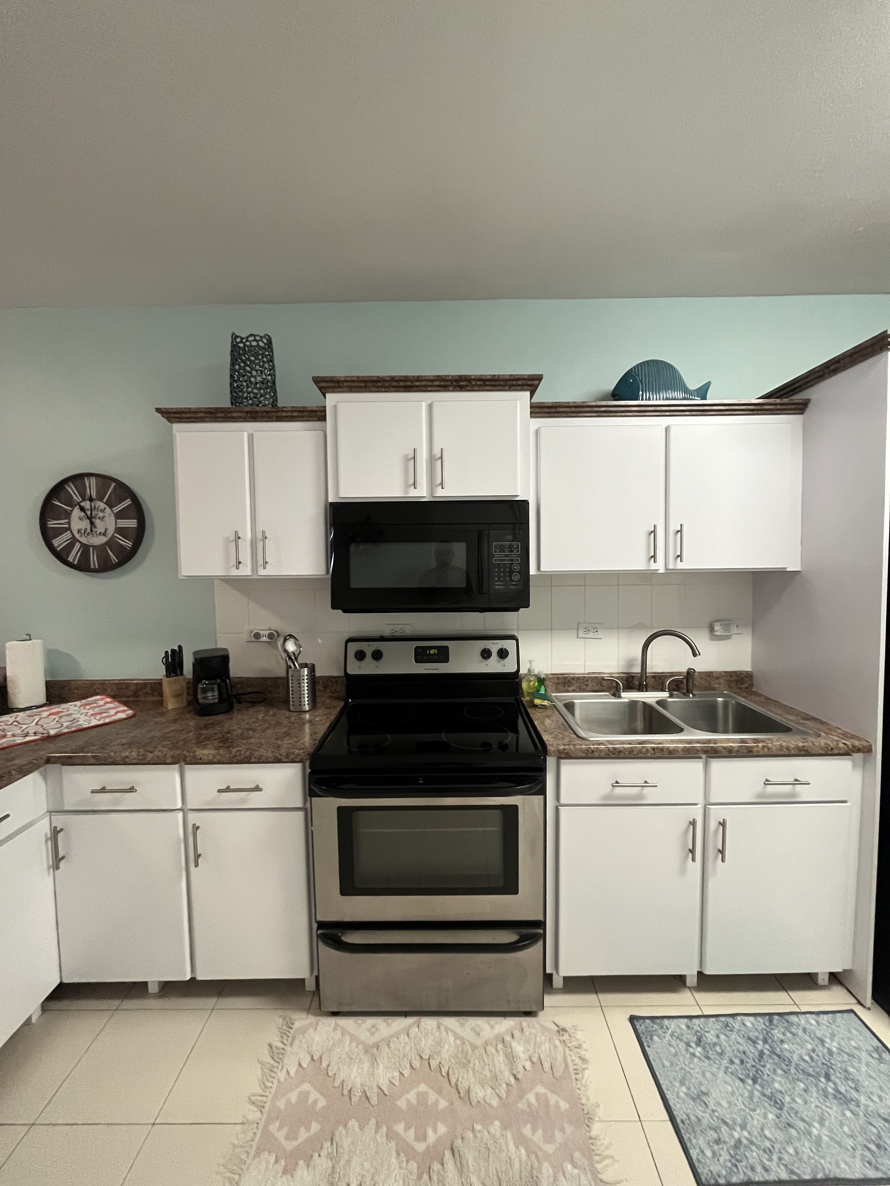 A kitchen with white cabinets, a black stove, a microwave, a sink, and a clock on the wall.