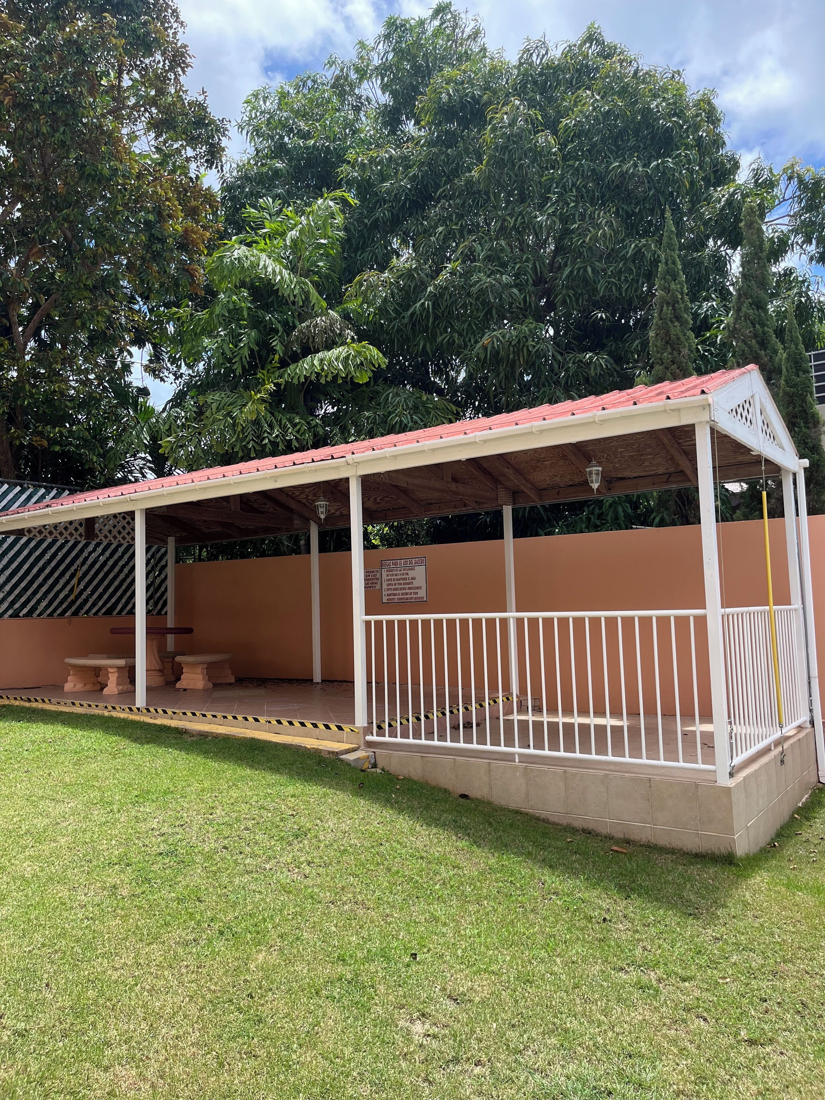 A covered outdoor seating area with a red roof, white railing, and a sign on the wall.
