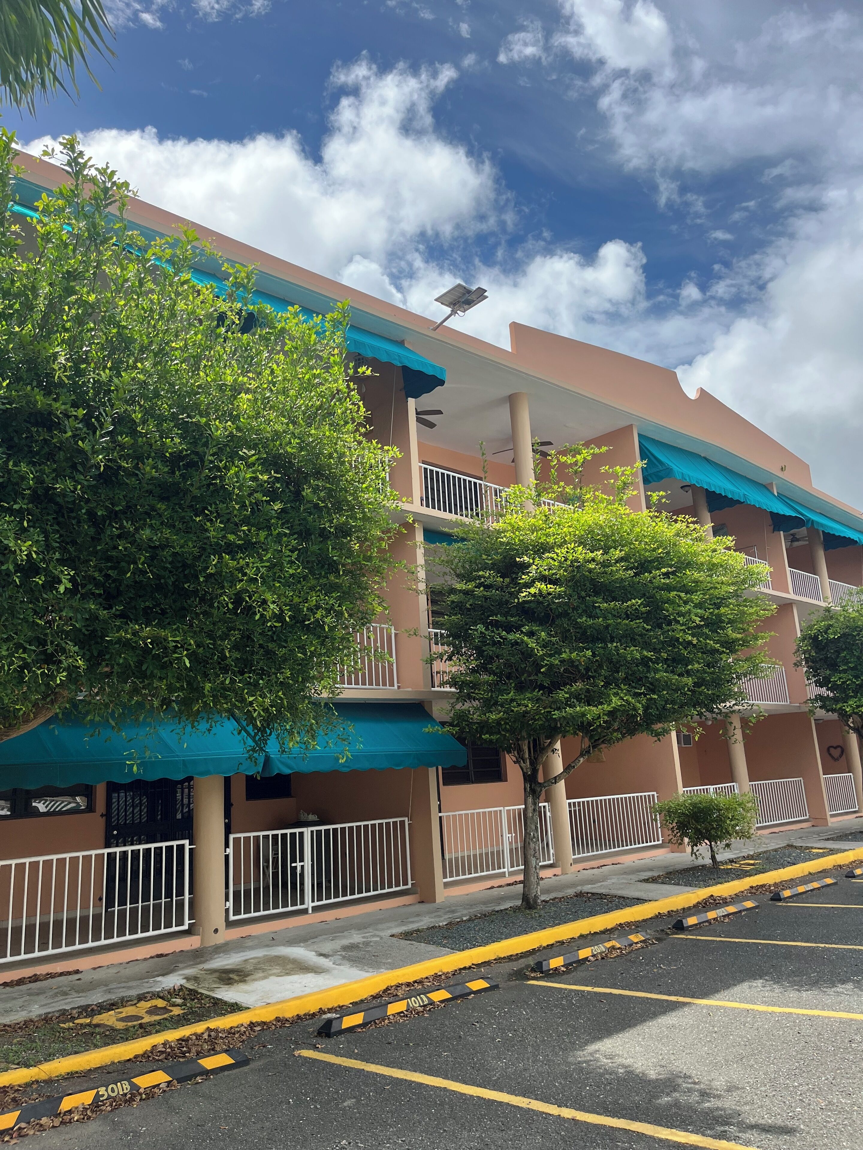 A multi-story building with balconies, a parking area with yellow lines, and a clear sky.