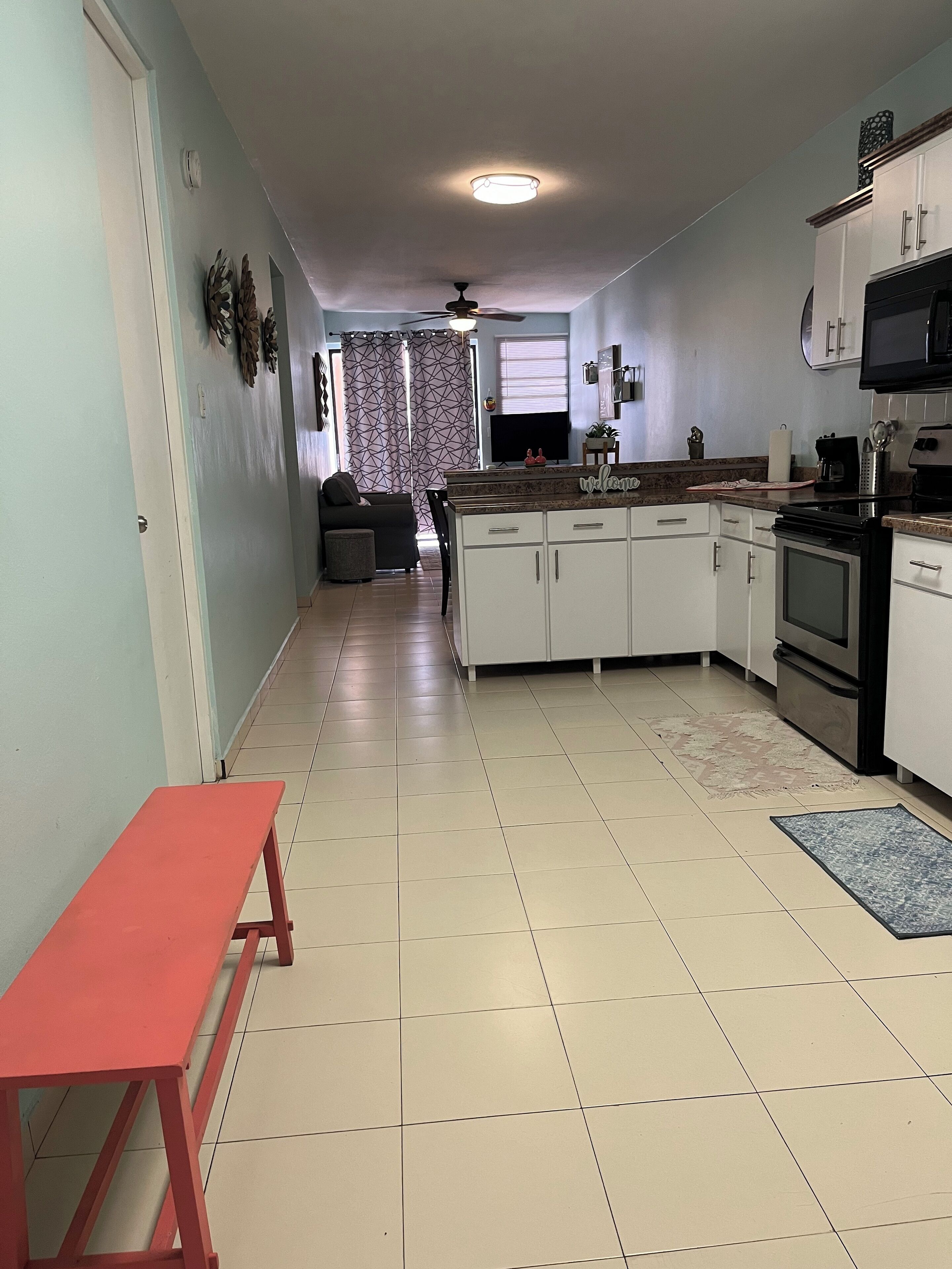 A compact kitchen with white cabinets, a built-in oven, and a microwave. A red bench is positioned in the foreground.