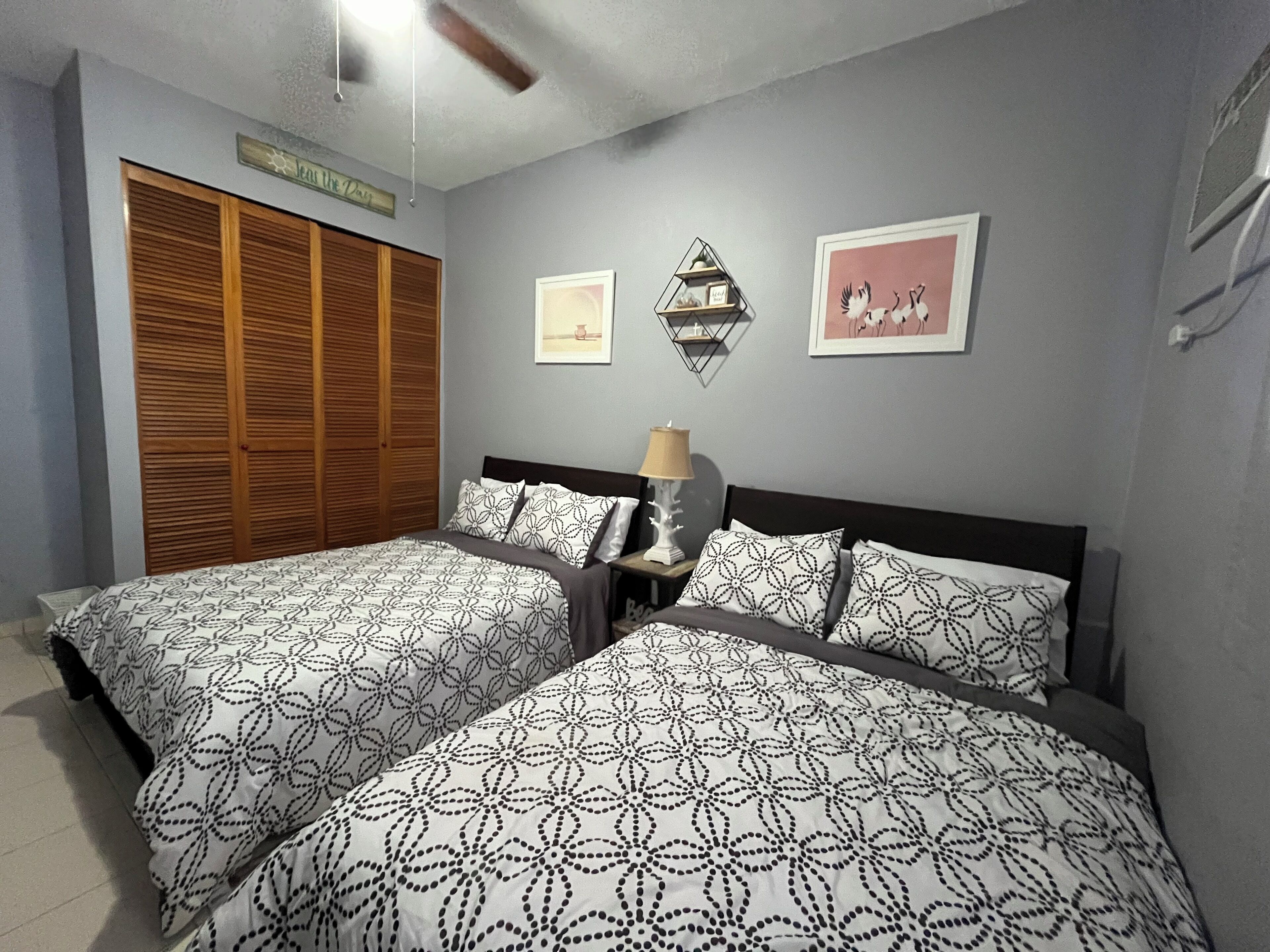 A bedroom with two beds, a wooden wardrobe, a wall-mounted shelf, and two framed pictures.