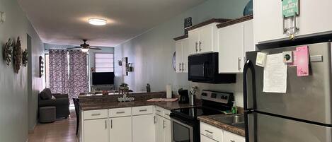 A compact kitchen with white cabinets, a black microwave, and a stainless steel refrigerator.