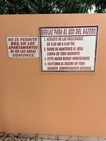 Dos carteles en una pared con normas para el uso del pabellón y prohibición de barbacoas en los apartamentos.