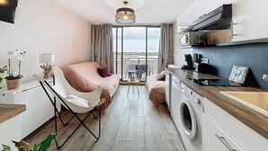 Een compacte hotelkamer met een bed, een wasmachine, een eethoek met tafel en stoelen, een klein keukenhoekje en uitzicht op de stad.