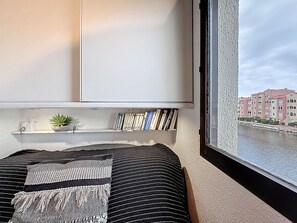 Ein Schlafzimmer mit einem Bett, einem Bücherregal, einem Fenster mit Blick auf Gebäude und einen Fluss.