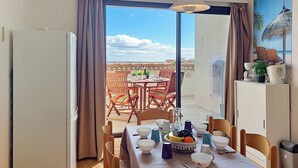 A dining area with a table set for two, a refrigerator, and a view of the terrace. - Coudalère/Guadeloupe by Interhome (Le Barcarès)