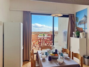 A dining area with a table set for two, a refrigerator, and a view of the terrace. - Coudalère/Guadeloupe by Interhome (Le Barcarès)