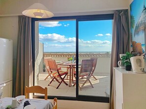 A room with a dining table, chairs, a refrigerator, and a view through a large sliding door to the outside. - Coudalère/Guadeloupe by Interhome (Le Barcarès)