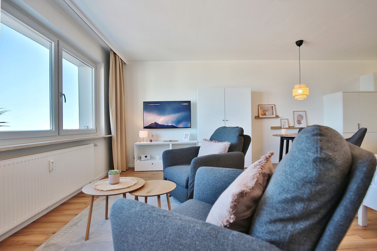 Uma sala de estar moderna com uma janela grande, uma TV de tela plana, um sofá, uma mesa de centro e uma escrivaninha com abajur.