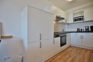 Eine moderne Küche mit weißen Schränken, einem eingebauten Backofen, einer Mikrowelle und einer Kaffeemaschine.