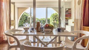A dining area with a table set for two, a bowl of fruit, and a bottle of drink. - Les Maisons sur la Plage by Interhome (Cap d'Agde)