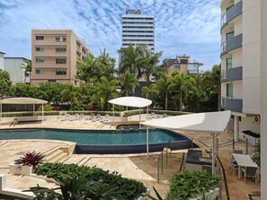 A rooftop pool area with lounge chairs, umbrellas, and a view of surrounding buildings.