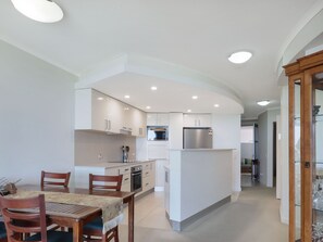 A modern kitchen with white cabinetry, a central island, and a dining area with a wooden table and chairs.