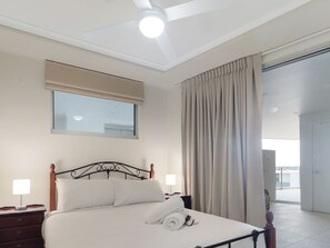 A hotel room with a bed, bedside lamps, a ceiling fan, a window with blinds, and a view of the outside.