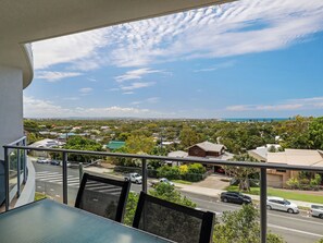 A balcony with a view of a residential area, a road with vehicles, and a distant coastline.
