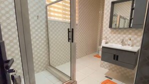 A modern bathroom with a glass shower door, a white sink, and a mirror above it. - DJ Villa Your Premium Stay-NF12 (Dawhenya)