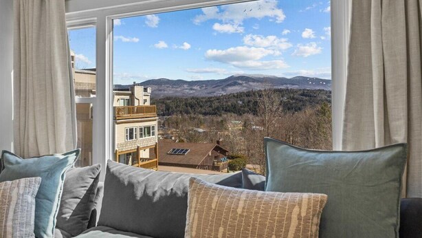 A room with a large window offering a view of a mountainous landscape and a building across the street.