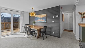 A dining area with a wooden table and chairs, a painting on the wall, and a view through a glass door to an outdoor deck.