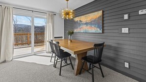 A dining area with a wooden table, four black chairs, a chandelier, and a painting on the wall.