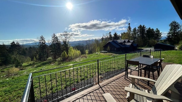 A deck with outdoor seating and a scenic view of a forest and mountains. - Gorgeous NEW Trapp Villa: Mountain View, Pool&More (Stowe)