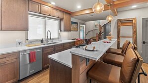 A modern kitchen with wooden cabinets, a central island, and a dining area with brown leather chairs. - Gorgeous NEW Trapp Villa: Mountain View, Pool&More (Stowe)