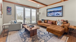 A living room with a sofa, coffee table, and a large window with a view of a snowy landscape. - Gorgeous NEW Trapp Villa: Mountain View, Pool&More (Stowe)