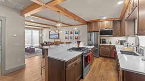 A modern kitchen with wooden beams, a central island, stainless steel appliances, and a dining area with a view. - Gorgeous NEW Trapp Villa: Mountain View, Pool&More (Stowe)