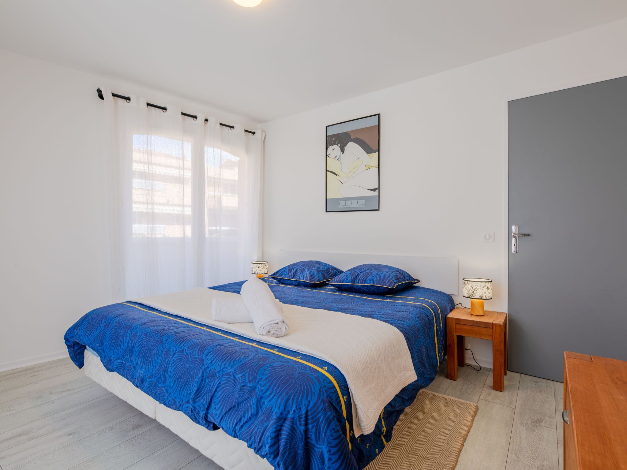 A bedroom with a bed, a nightstand, a lamp, a door, and a window with curtains.
