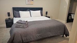 A neatly made bed with a grey duvet, two bedside tables with lamps, and a folded grey blanket on the bed.