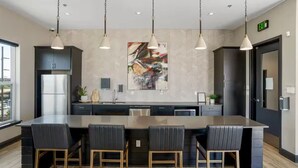 Une cuisine moderne dotée d’un grand îlot central, de meubles de couleur noire, d’appareils électroménagers en acier inoxydable et de luminaires suspendus.