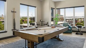 Une table de billard dans une pièce moderne avec de grandes fenêtres, une vue sur la ville et un coin salon décontracté.