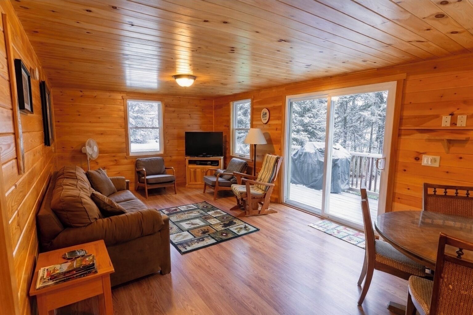 Un intérieur de chalet chaleureux avec un plancher en bois, un canapé, un téléviseur et un coin repas.