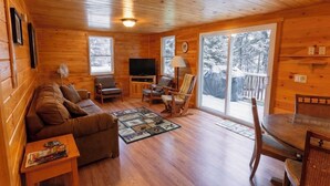 Un interior de cabaña acogedor con piso de madera, un sofá, un televisor y una zona de comedor.
