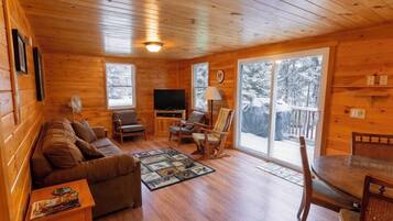 Un intérieur de chalet chaleureux avec un plancher en bois, un canapé, un téléviseur et un coin repas.