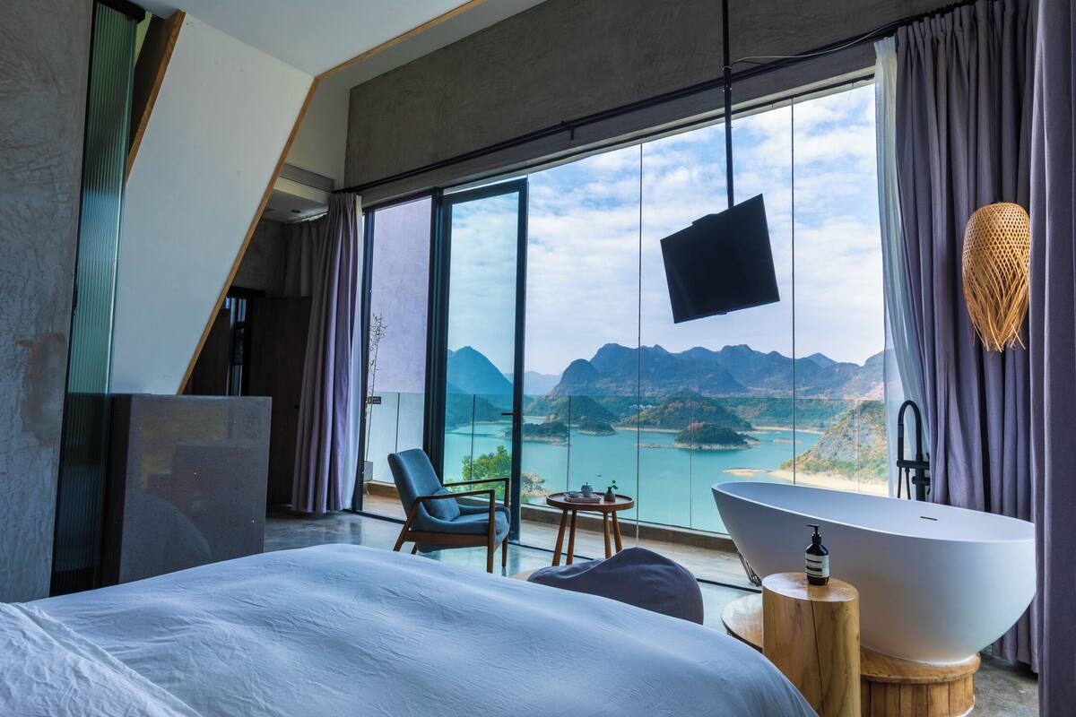 Ett modernt hotellrum med en stor säng, ett badkar, en stol och ett bord.