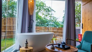 Un baño moderno con una bañera grande, un taburete de madera, una mesa con bandeja y una silla.