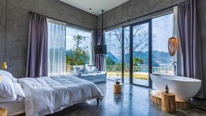 Un dormitorio moderno con una cama grande, una bañera independiente y vistas a montañas a través de amplios ventanales.
