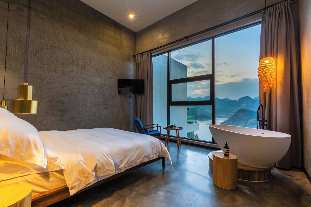 Ett modernt hotellrum med en stor säng, ett badkar, en TV och utsikt över bergen.