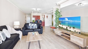A modern living room with a black sofa, a coffee table, and a large flat-screen TV displaying a beach scene. - Chevron Renaissance Ocean View (Surfers Paradise)