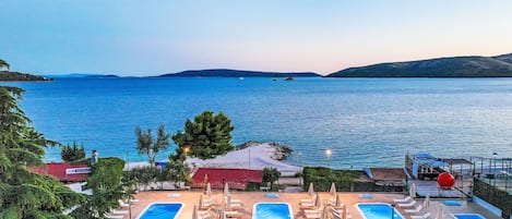 A resort with two swimming pools, lounge chairs, and umbrellas.