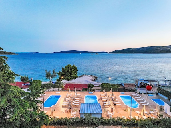 A resort with two swimming pools, lounge chairs, and umbrellas.