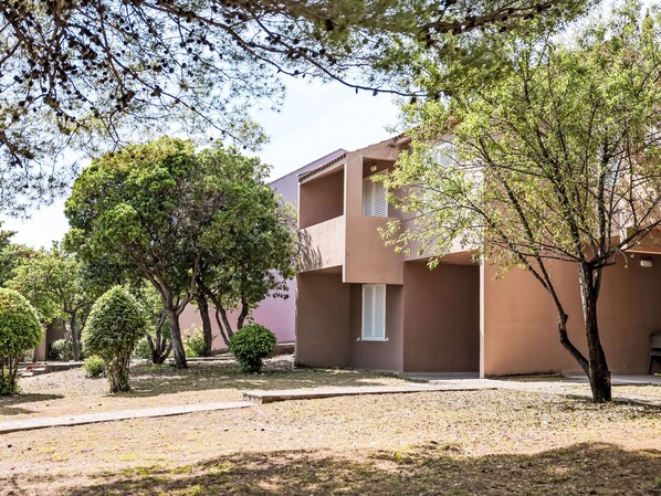 A building with a flat roof and a balcony, surrounded by trees and a grassy area.