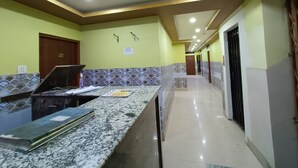 Corridoio di un hotel con reception, ventilatore a soffitto, pareti piastrellate e un lungo corridoio che conduce a delle porte.