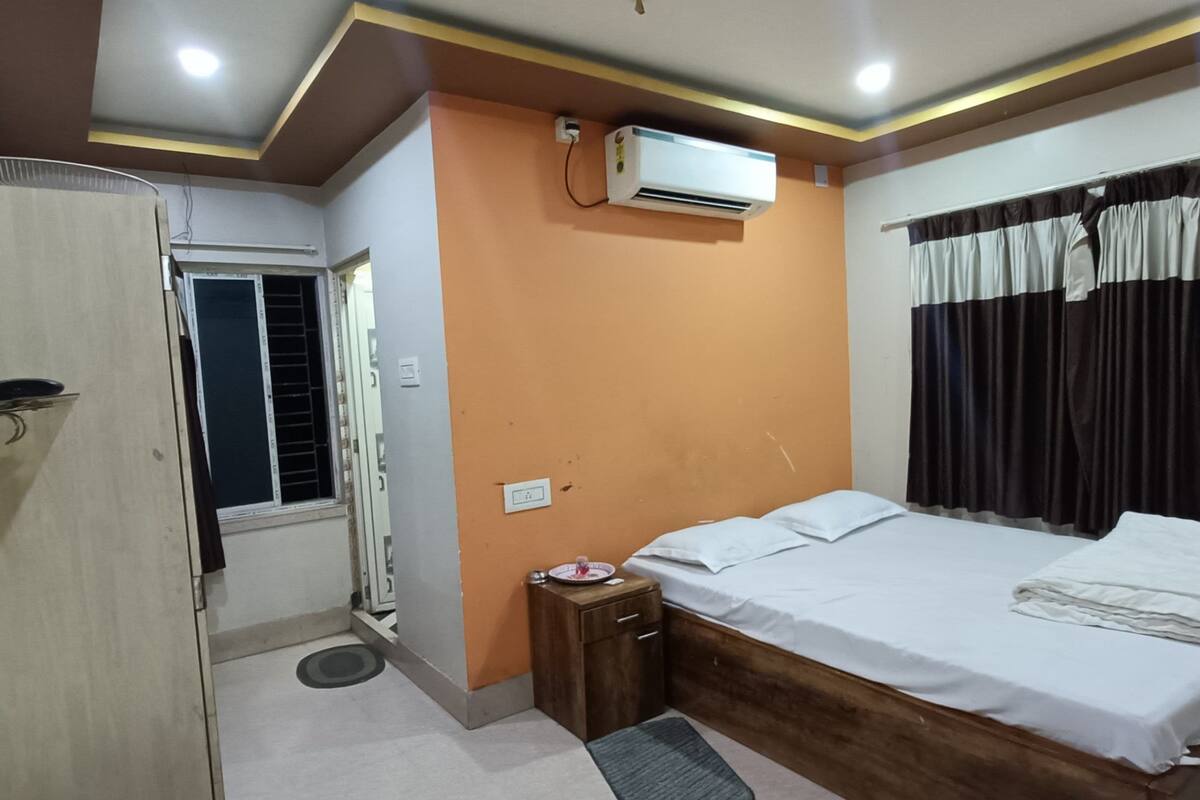 A bedroom with a bed, wardrobe, air conditioning unit, and a small table.