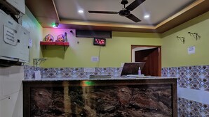 Un'area reception con un bancone in marmo, una ventola a soffitto, un televisore e un cartello che indica il divieto di portare cibo dall'esterno.