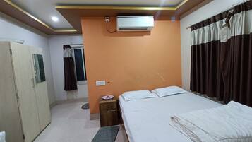 Habitación de hotel con cama, armario, mesita pequeña, equipo de aire acondicionado y ventana con cortinas.